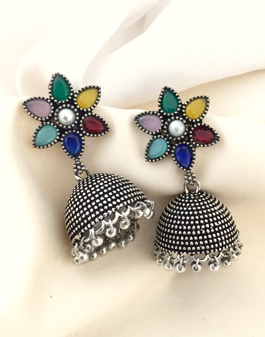 A pair of silver jhumka earrings with intricate detailing and colorful floral tops.