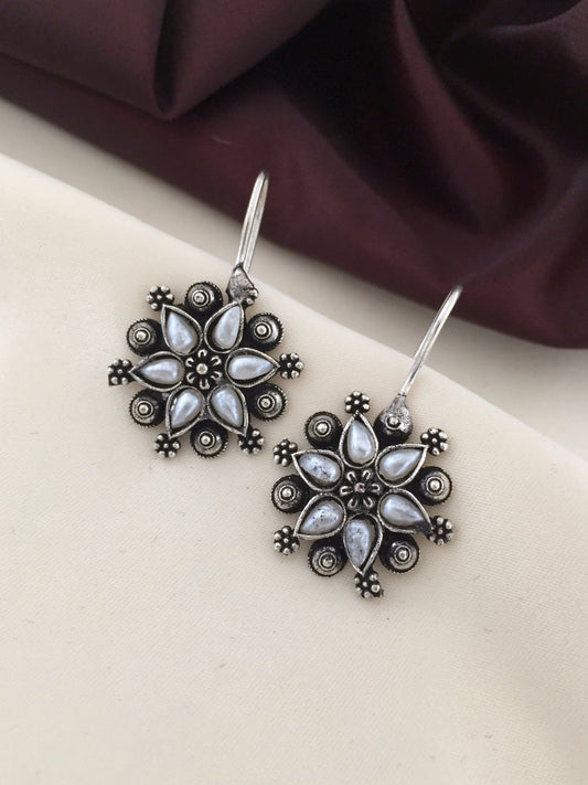 A pair of silver floral earrings with intricate detailing and white gemstone accents.
