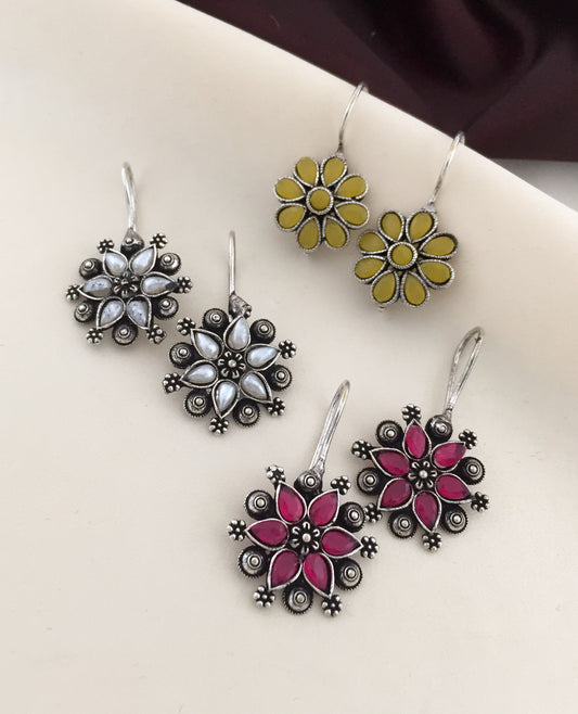 Three pairs of floral design earrings in silver, yellow, and pink.