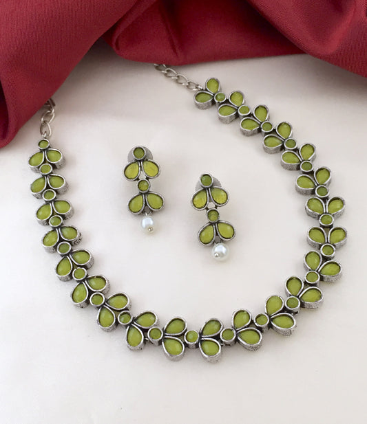 A necklace and matching earrings set featuring green petal-shaped stones and silver accents. The earrings have a dangling pearl at the bottom.