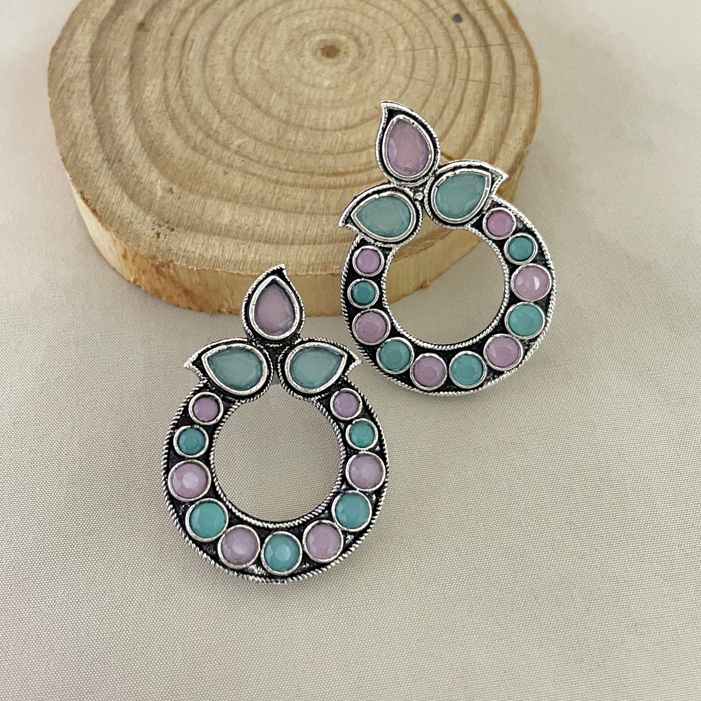 A pair of circular earrings with a combination of purple and green stones set in a silver frame.