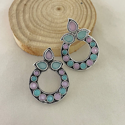 A pair of circular earrings with a combination of purple and green stones set in a silver frame.