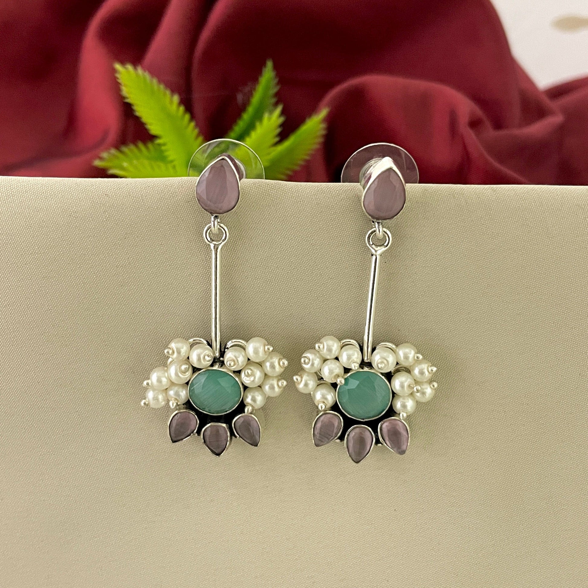 Silver dangle earrings with purple and green gemstones, pearl accents, and floral design.
