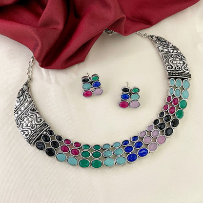 A silver necklace with intricate designs and colorful gemstones, accompanied by matching earrings.