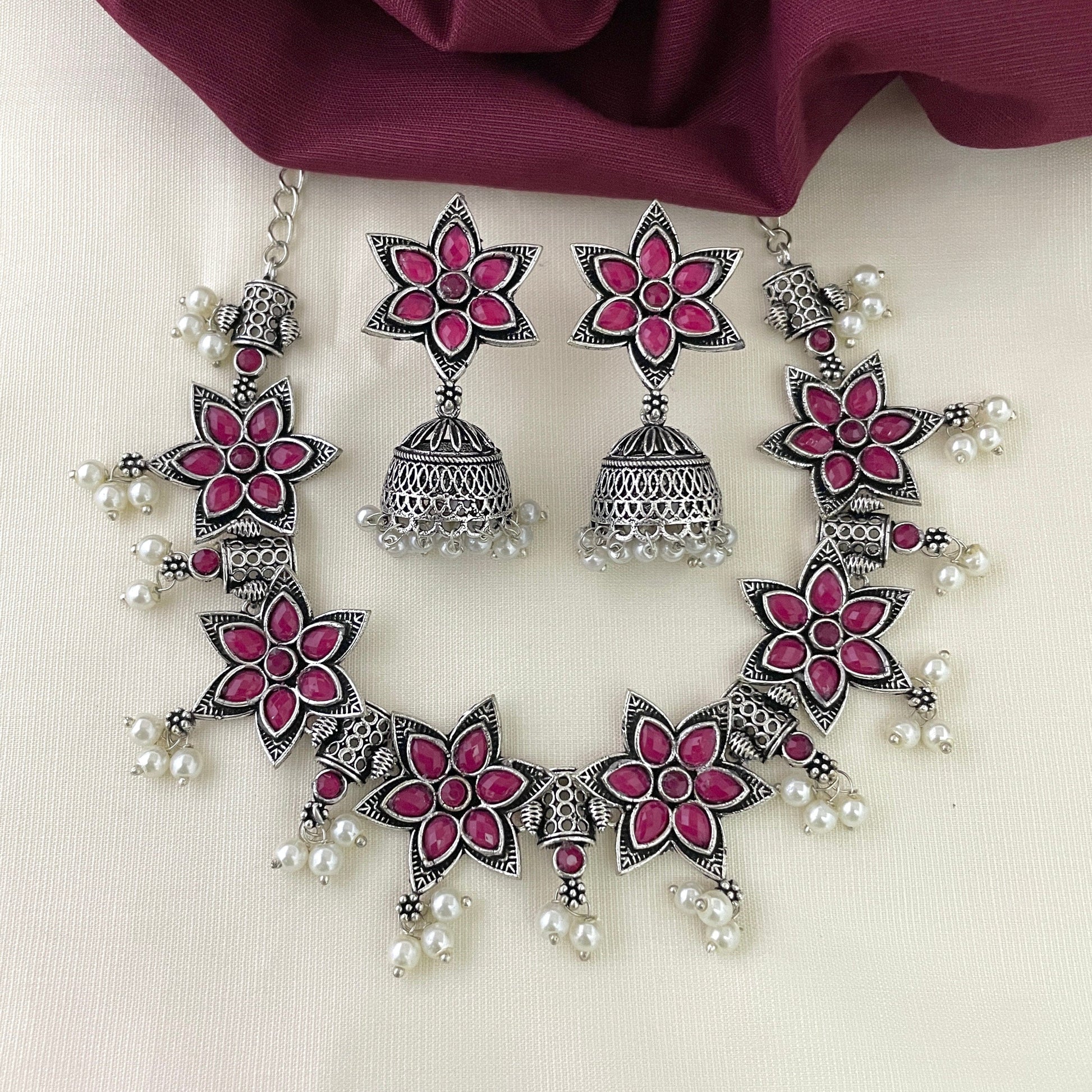 A silver necklace and earring set featuring pink floral designs and pearl accents.