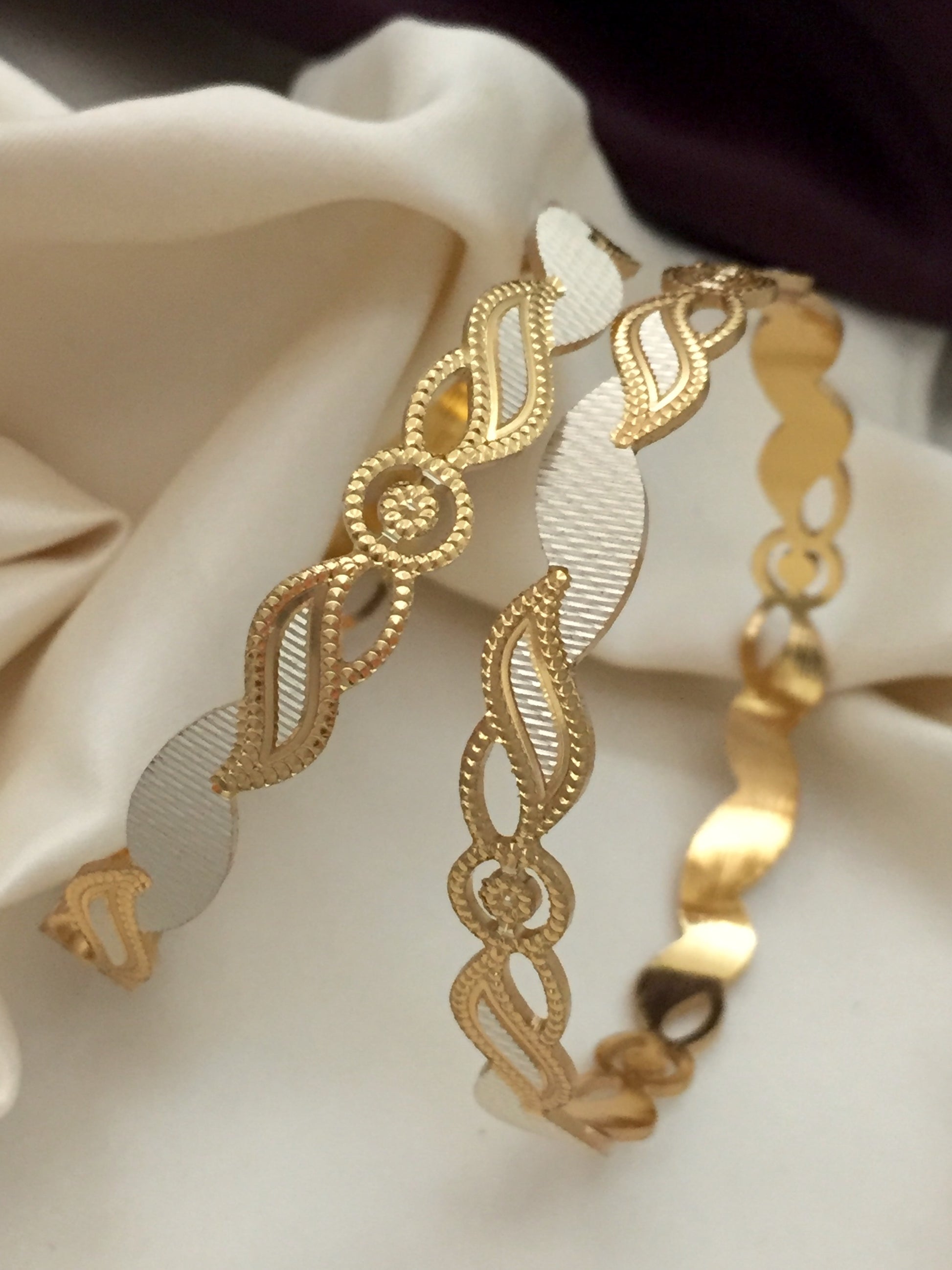 Two gold bracelets with intricate designs and white accents.