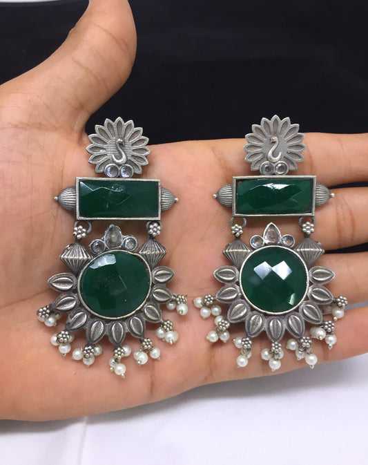 A pair of silver earrings with green gemstones and intricate floral designs.