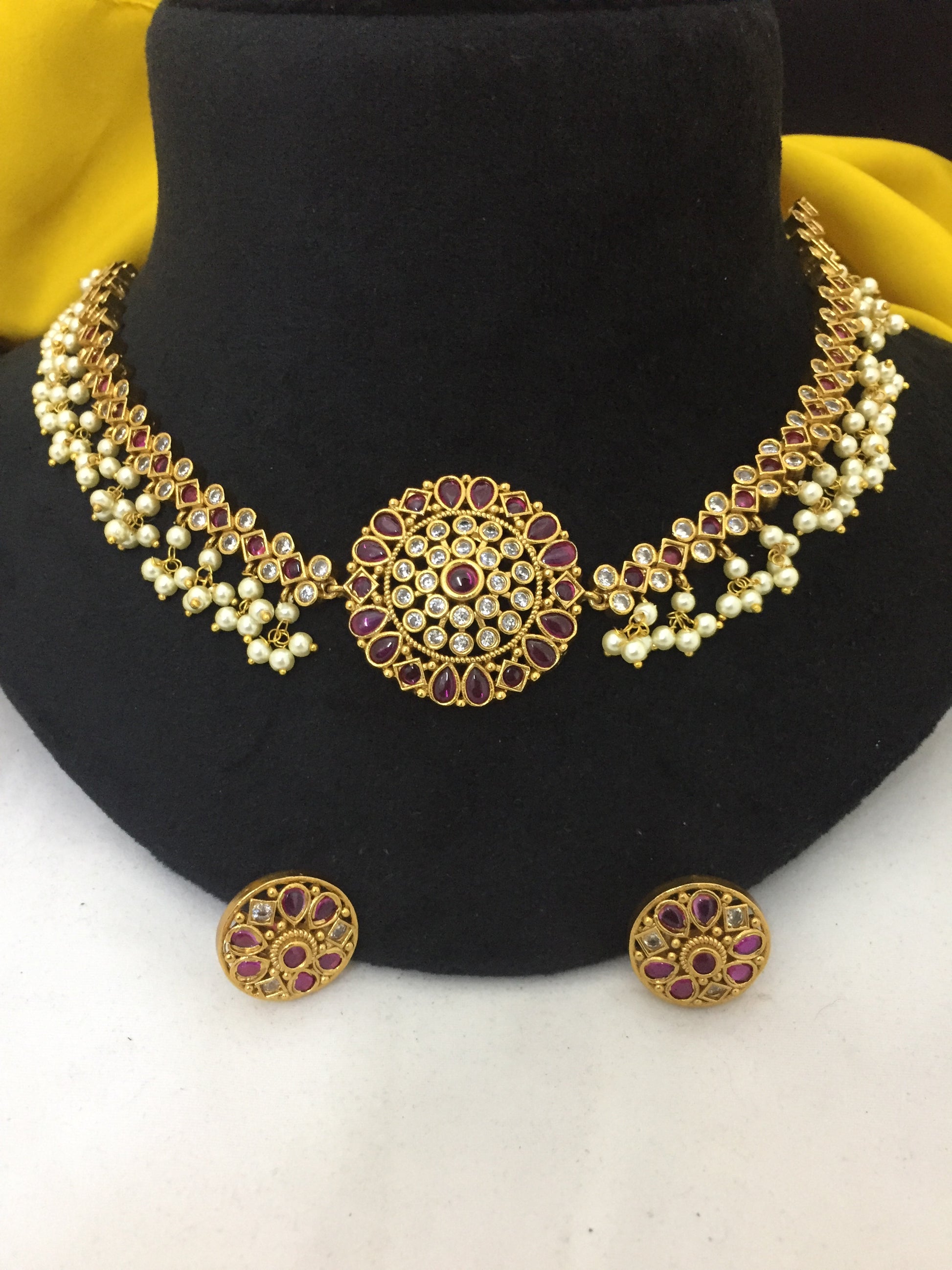 Gold necklace with intricate design featuring purple gemstones and pearls, accompanied by matching round earrings.