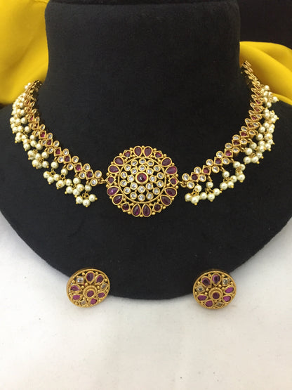 Gold necklace with intricate design featuring purple gemstones and pearls, accompanied by matching round earrings.