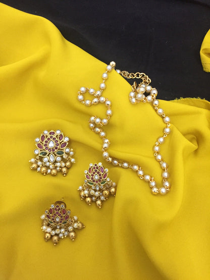 A set of traditional jewelry featuring a pearl necklace and three ornate earrings with gold, red, and green detailing.