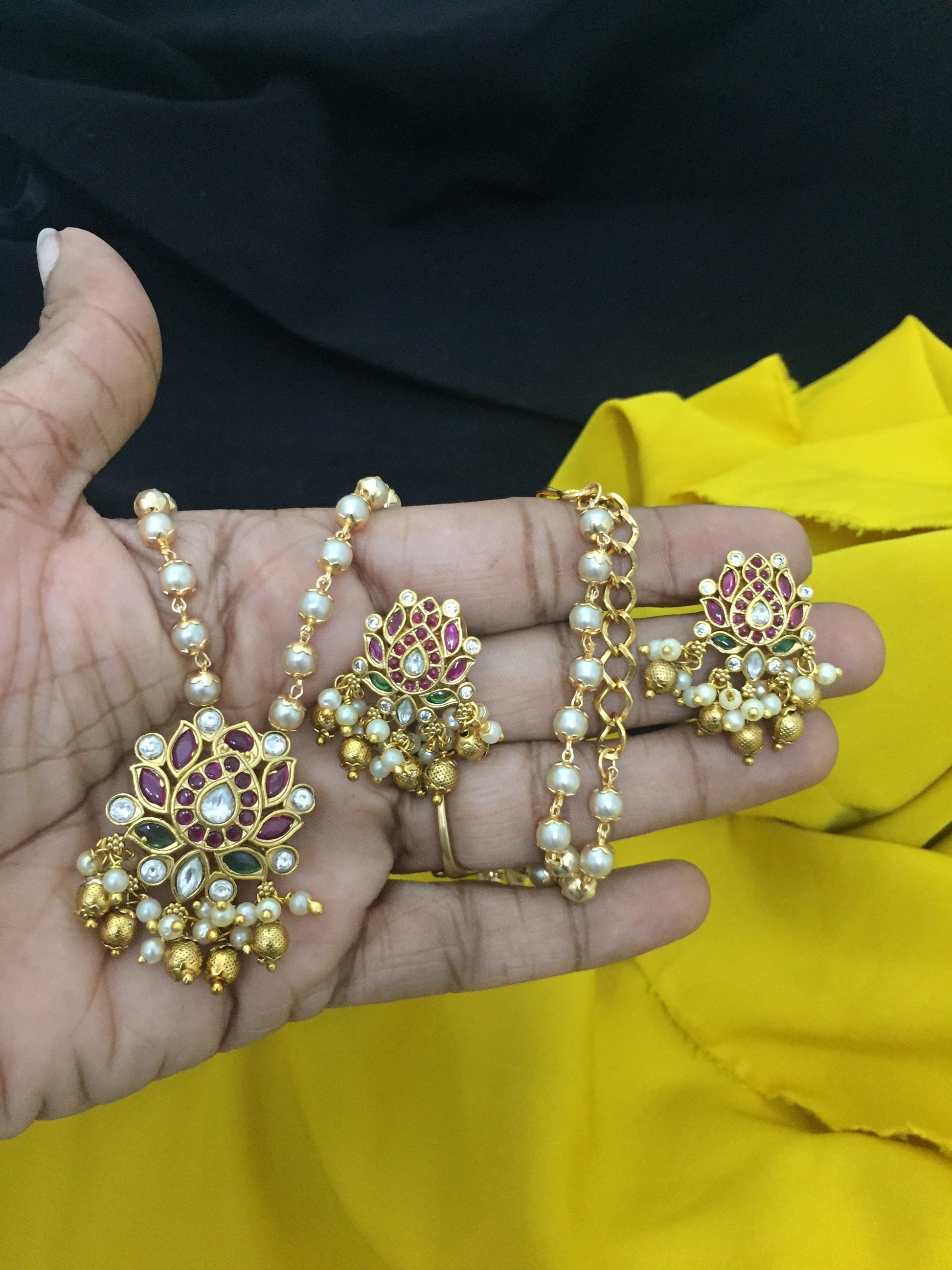 A hand holding a set of traditional jewelry, including a necklace and matching earrings, adorned with pearls, gold beads, and intricate floral designs.