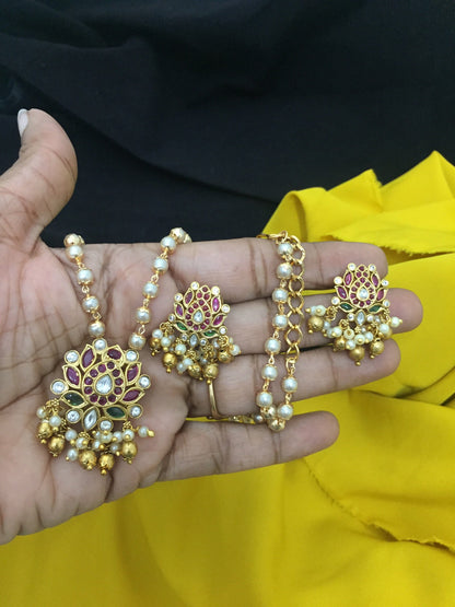 A hand holding a set of traditional jewelry, including a necklace and matching earrings, adorned with pearls, gold beads, and intricate floral designs.