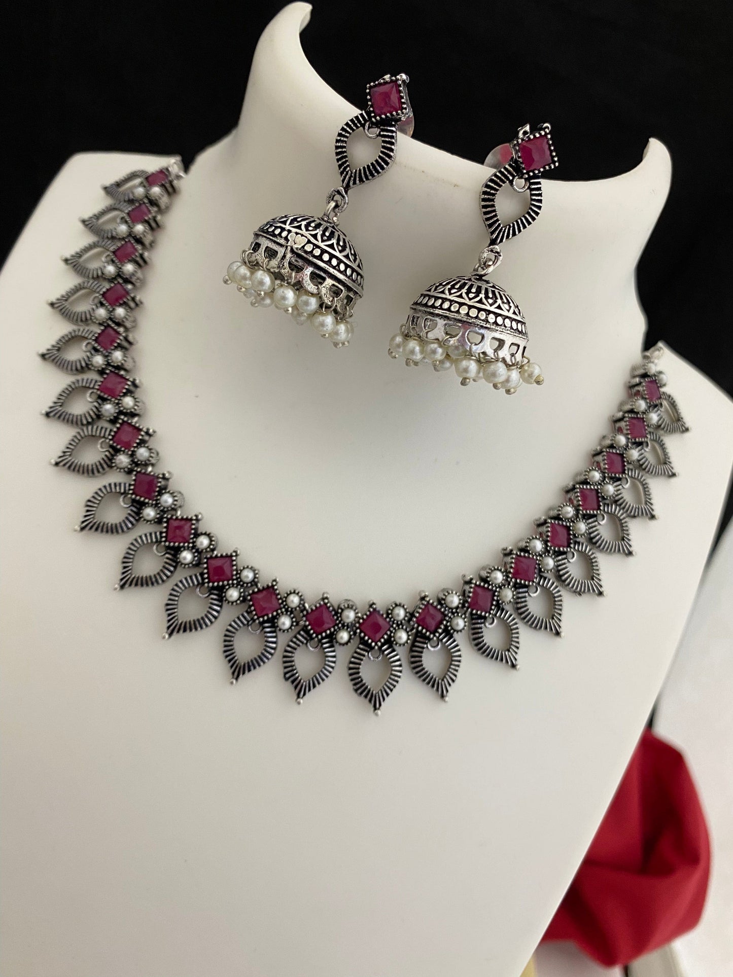 Silver necklace with red gemstones and matching jhumka earrings with pearl accents.