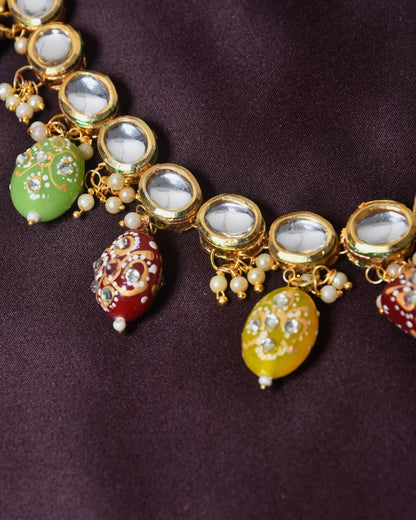 A close-up of a gold necklace with oval-shaped mirror embellishments and colorful, intricately designed beads hanging from it.