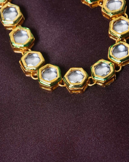 A close-up of a gold necklace with hexagonal-shaped links, each containing a clear gemstone.