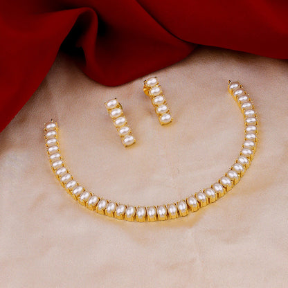 A gold and pearl jewelry set with a necklace and matching earrings displayed on a beige fabric with a red cloth in the background.