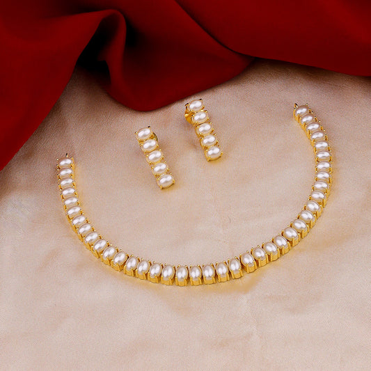 A gold and pearl jewelry set with a necklace and matching earrings displayed on a beige fabric with a red cloth in the background.