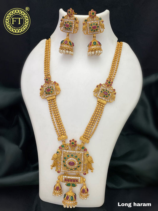 Gold long haram necklace set with intricate designs, featuring red and green gemstones, and matching earrings.