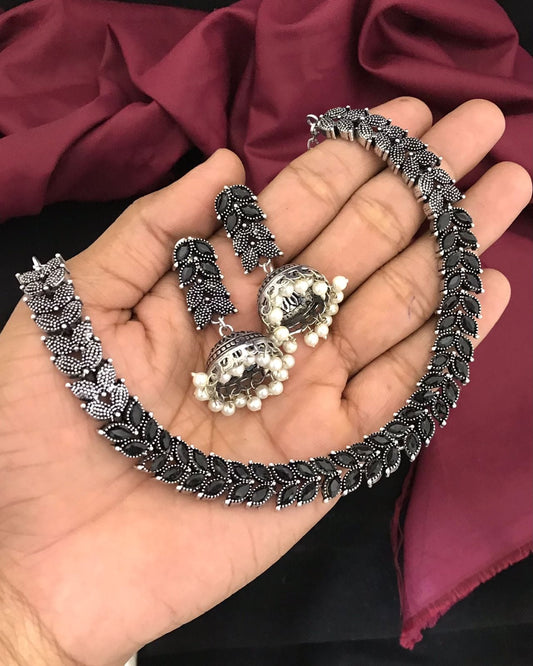 A hand holding a silver oxidized jewelry set consisting of a choker necklace and matching earrings.