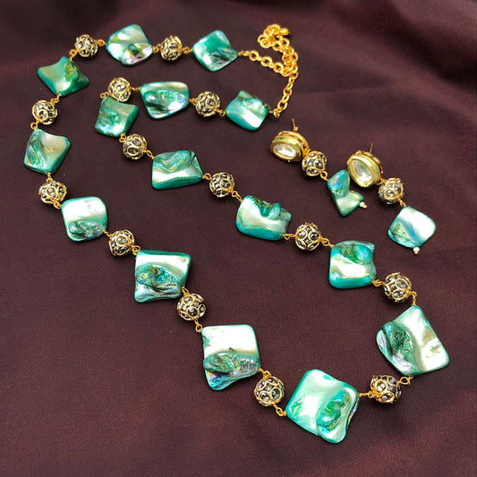 A necklace with square green and white marbled beads and gold filigree beads, laid out on a dark fabric background.