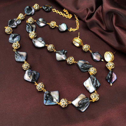 A necklace and earrings set featuring black and white iridescent shell pieces and gold filigree beads, displayed on a dark maroon fabric background.