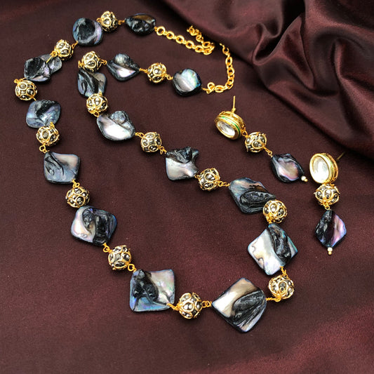 A necklace and earrings set featuring black and white iridescent shell pieces and gold filigree beads, displayed on a dark maroon fabric background.