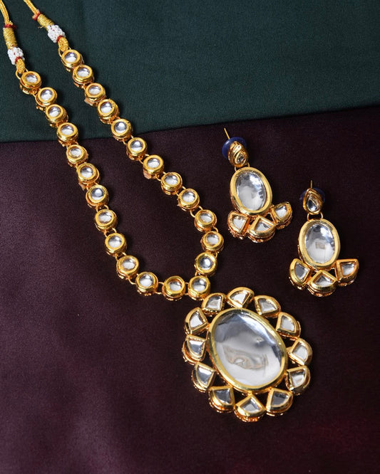 A gold necklace with matching earrings and a large pendant, all adorned with white gemstones.