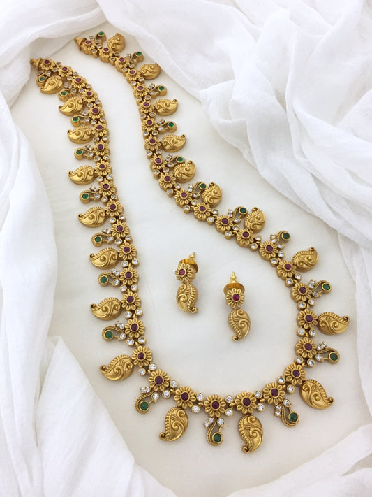 A gold necklace set with intricate designs, featuring red, green, and white stones, accompanied by matching earrings.