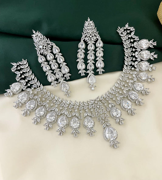 A silver necklace and matching earrings set with intricate designs and large, clear gemstones.