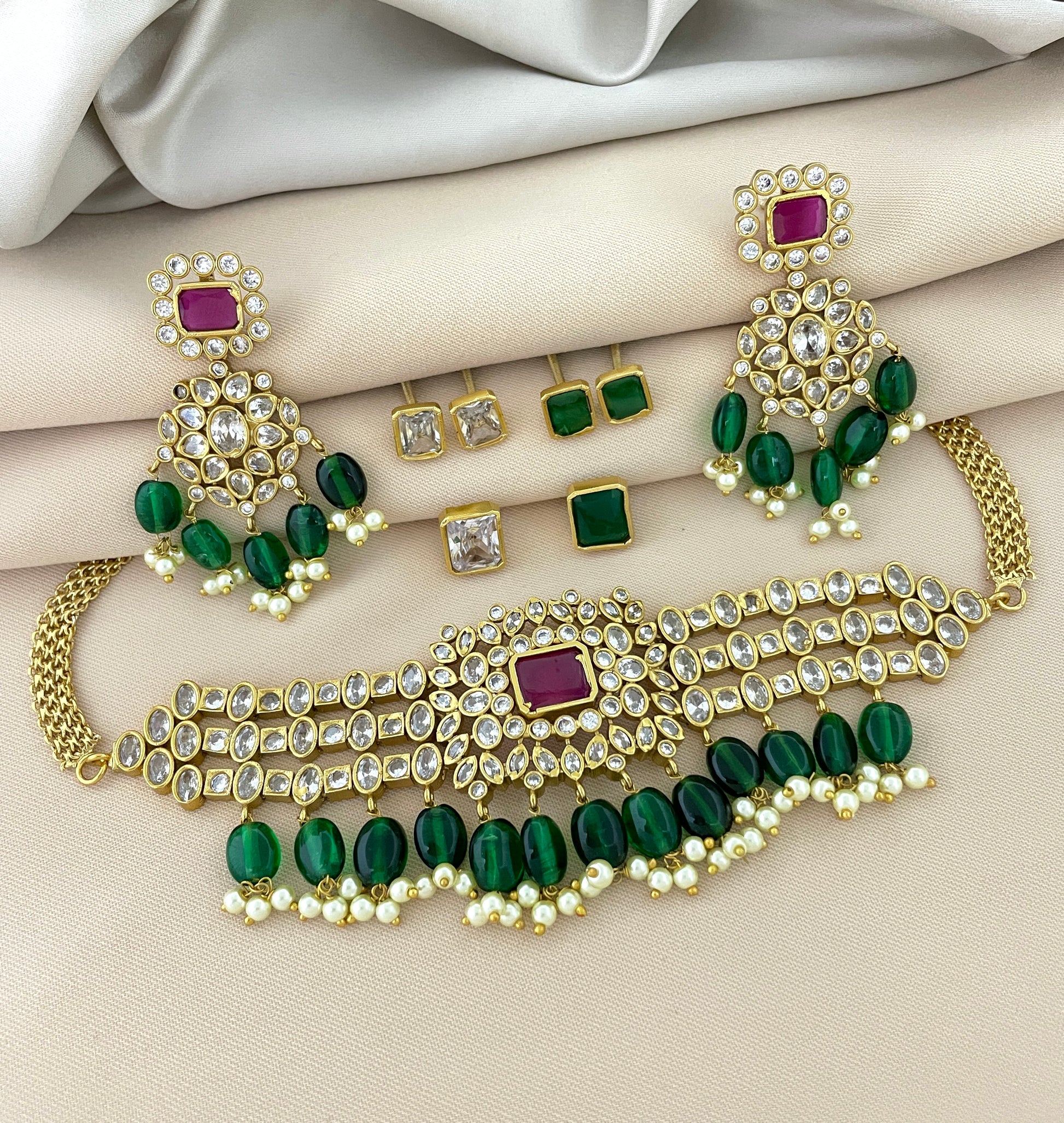 A gold jewelry set featuring a choker necklace with green and white stones, matching earrings, and additional stud earrings.