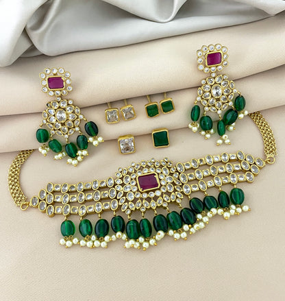 A gold jewelry set featuring a choker necklace with green and white stones, matching earrings, and additional stud earrings.