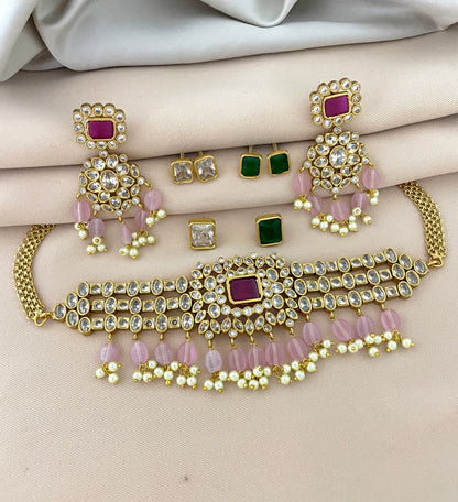 A gold jewelry set featuring a choker necklace with pink and white beads, matching earrings with pink and white beads, and additional stud earrings with green and clear stones.