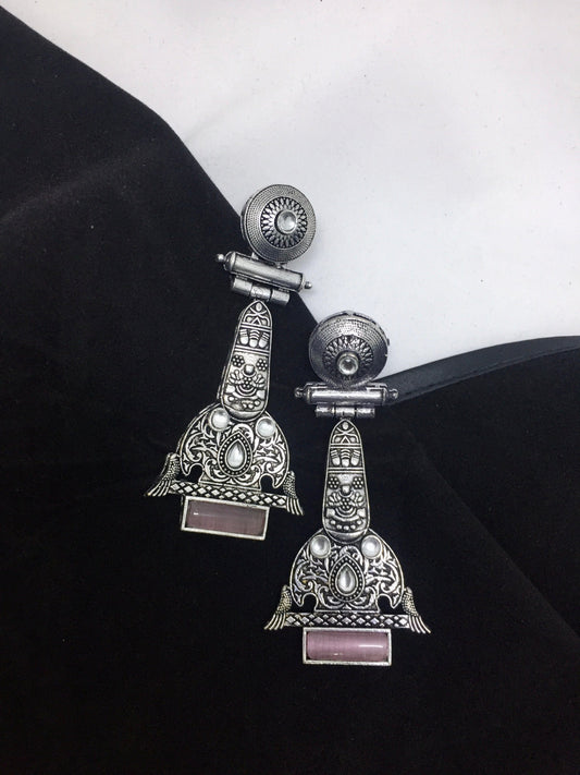 A pair of intricately designed silver earrings with detailed engravings and pink rectangular stones at the bottom.
