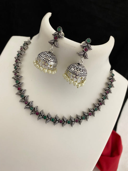 Silver necklace and earrings set with intricate designs, featuring green and red stones and pearl accents.