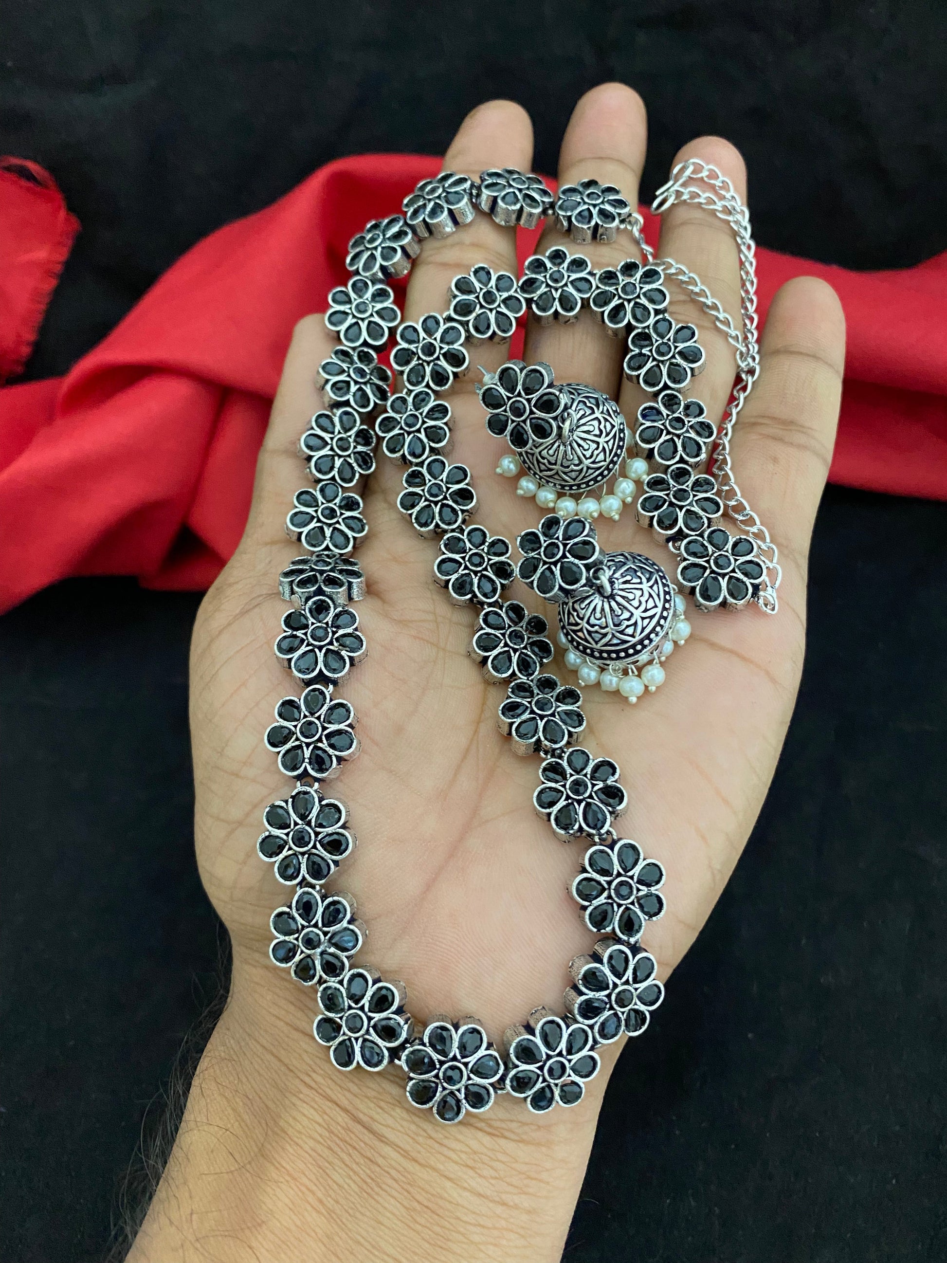 A hand holding a silver floral necklace and matching earrings.
