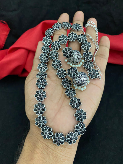 A hand holding a silver floral necklace and matching earrings.
