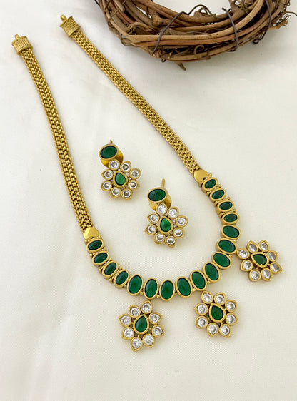 A gold necklace with green oval stones and matching earrings featuring green and white stones.