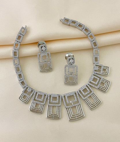 A silver necklace with geometric designs and matching earrings adorned with American diamonds.