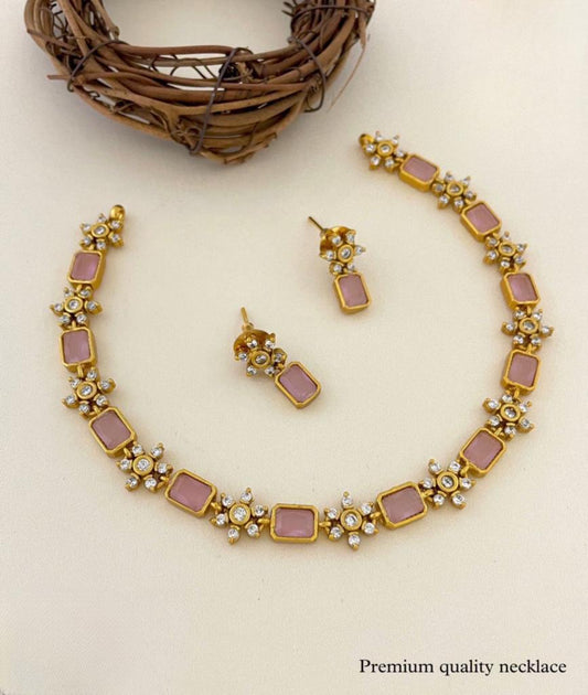 A handcrafted necklace with a matte finish in soft pink, featuring rectangular pink stones and floral designs, accompanied by matching earrings.
