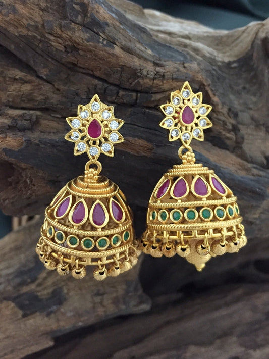 Gold-plated jhumka earrings with red and green stones and intricate design.