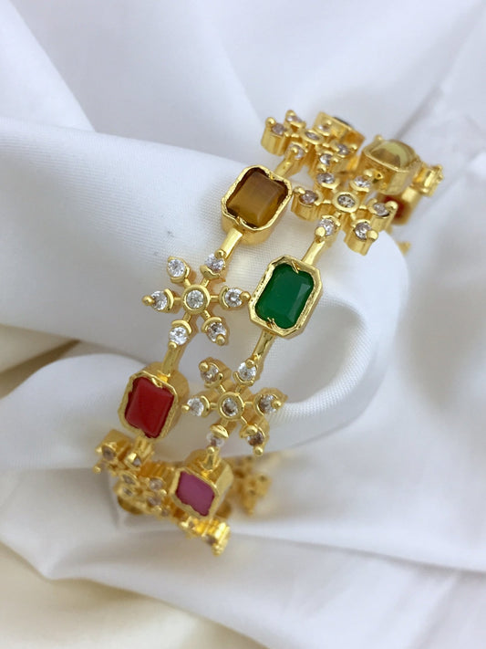 Gold bangles adorned with colorful Navratna stones and small white crystals.