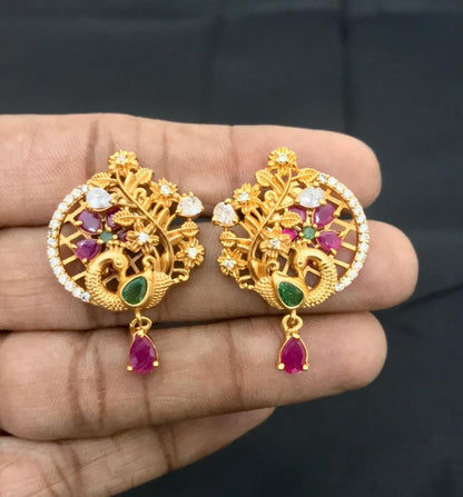Gold stud earrings with intricate peacock design, adorned with rubies, emeralds, and diamonds, featuring a hanging ruby teardrop.
